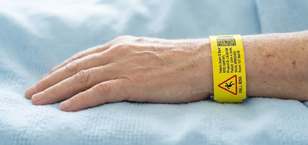 Close-up of a yellow color-coded patient safety wristband indicating a fall risk alert in a dignified mental health environment.

