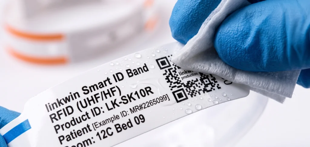 Medical thermal wristband being disinfected with an alcohol swab to demonstrate sanitizer resistance for infection control standards.
